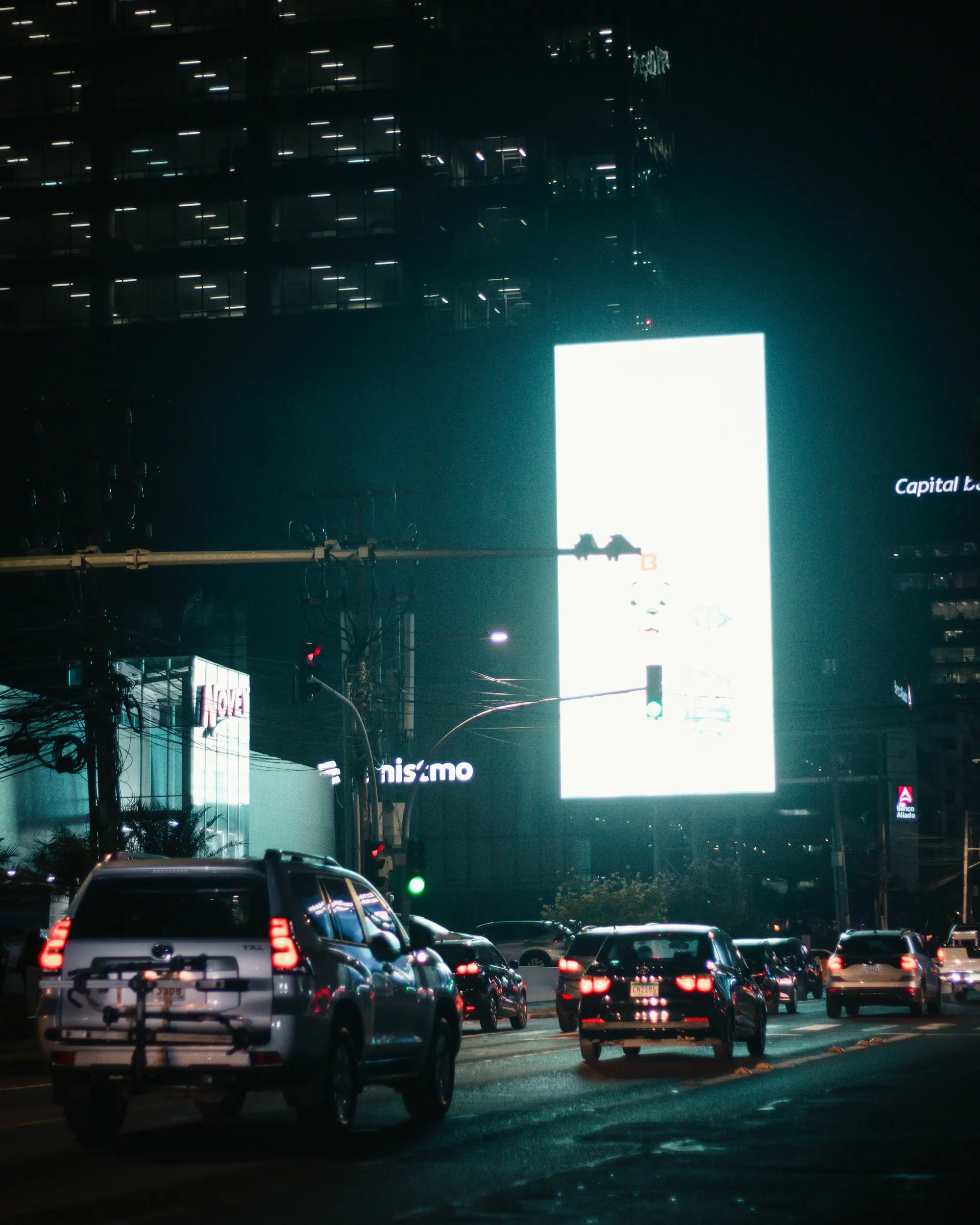 Painel de LED aceso sobre uma avenida à noite, com o trânsito passando embaixo.